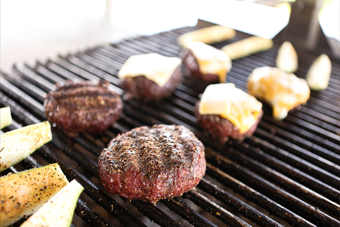 Thick-cut seasoned steaks cooking on a grill with visible smoke, capturing the rich texture and flavor of Drummond Ranch’s premium cuts.