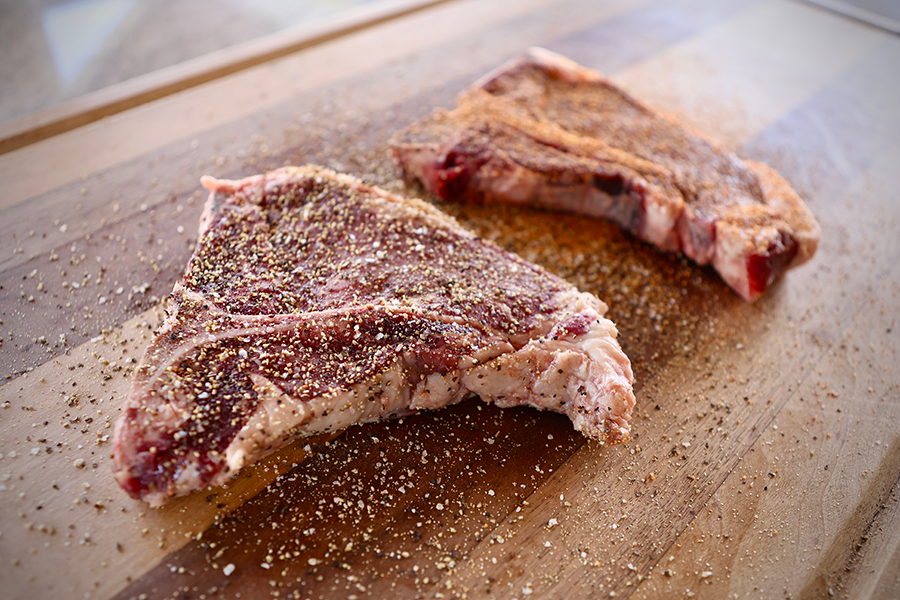 Two seared steaks sizzling on a flat-top grill surrounded by golden-brown potato wedges, showcasing a hearty Drummond Ranch meal in progress.